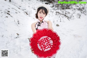 A woman in a pink dress is posing in the snow.